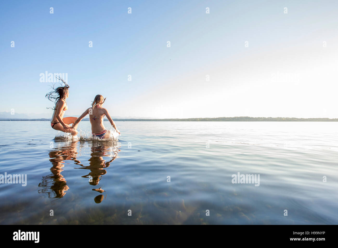 Two young women jumping into lake Stock Photo