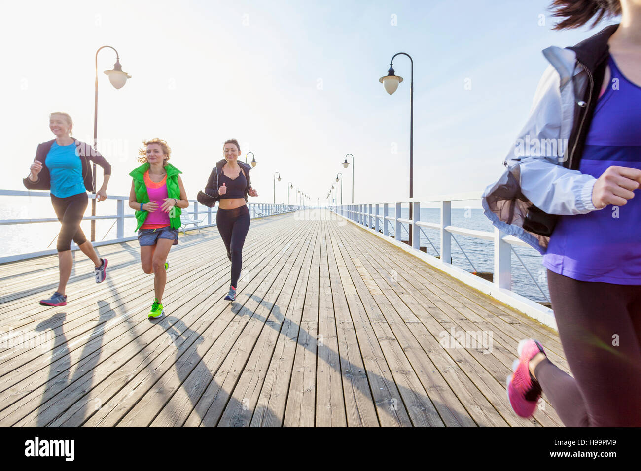 Group of women in sports clothing running on jetty Stock Photo
