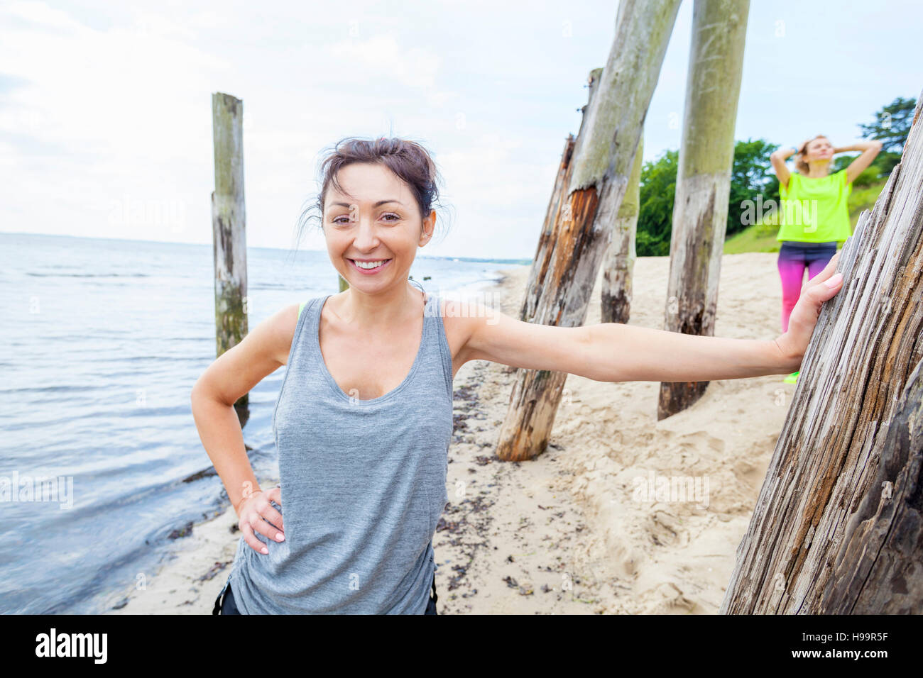 Woman in tank top on beach leaning against wooden post Stock Photo