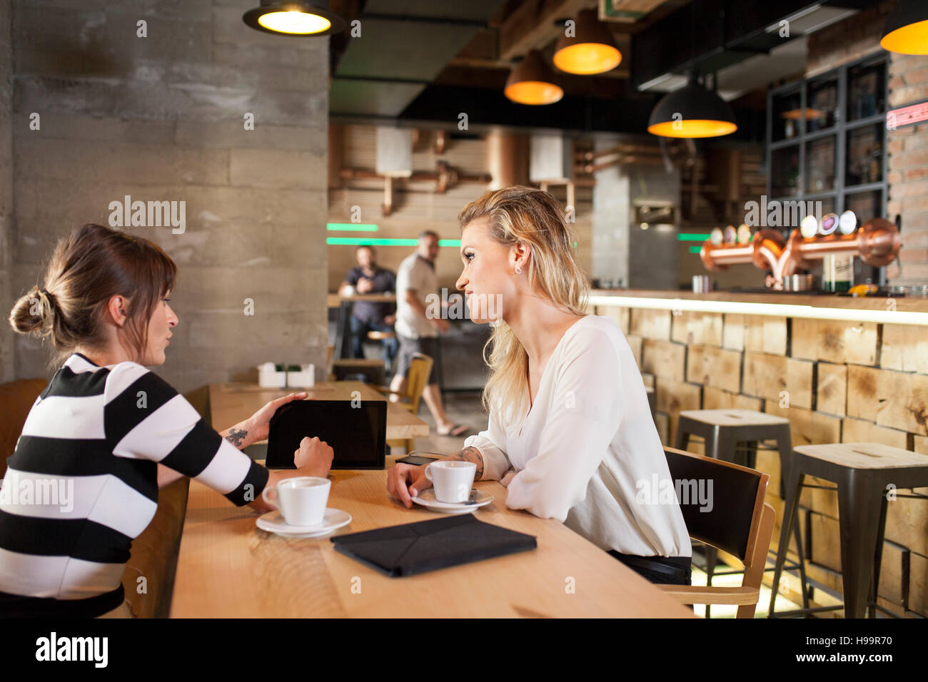 Two girlfriends in coffee shop looking at digital tablet Stock Photo