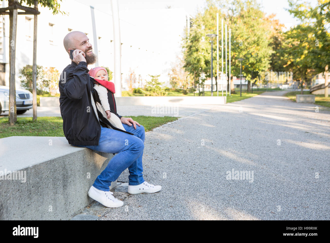 Father with baby girl in baby carrier using phone Stock Photo