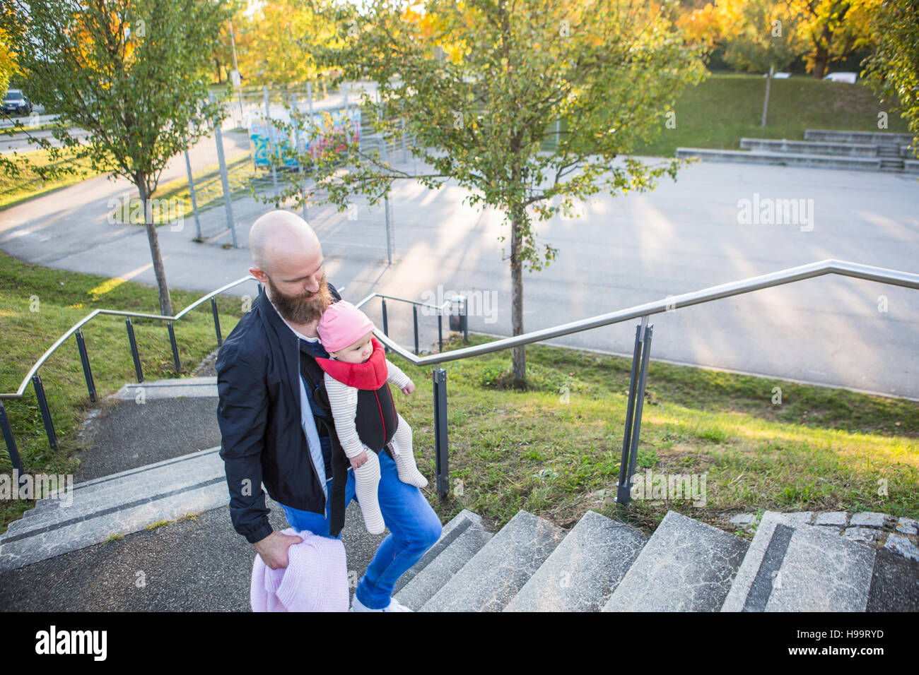 Father with baby girl in baby carrier walking up steps Stock Photo