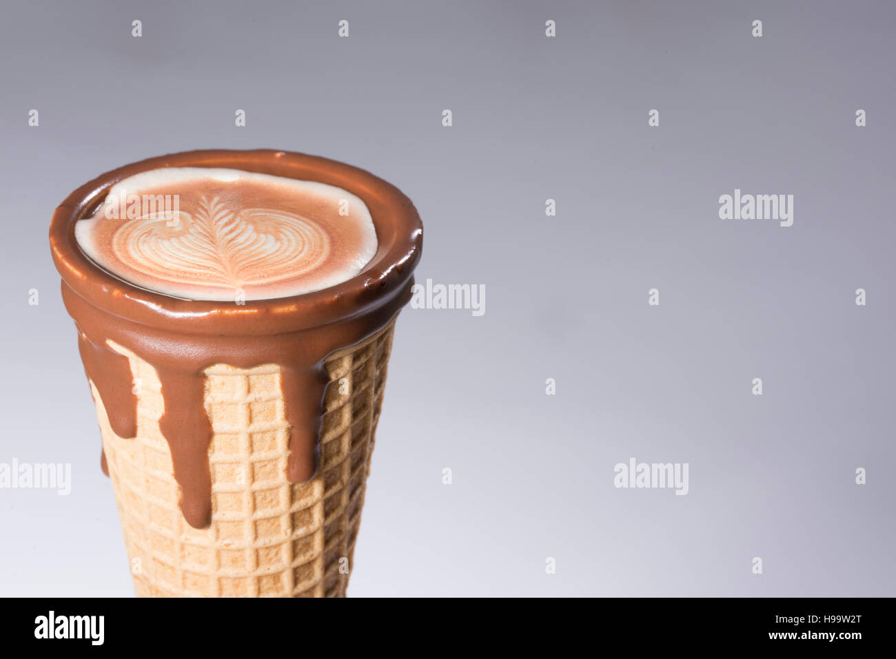 Coffee in waffle cone dipped in chocolate with drawings in cappuccino / latte milk foam, latte art, isolated Stock Photo