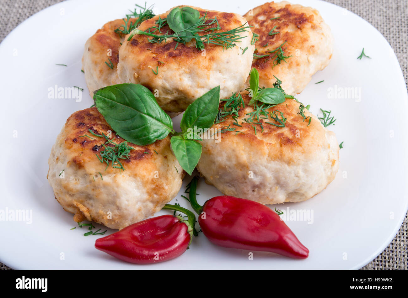 Close Up view on rissole of minced chicken meat on a white plate with red pepper and basil on sackcloth background Stock Photo
