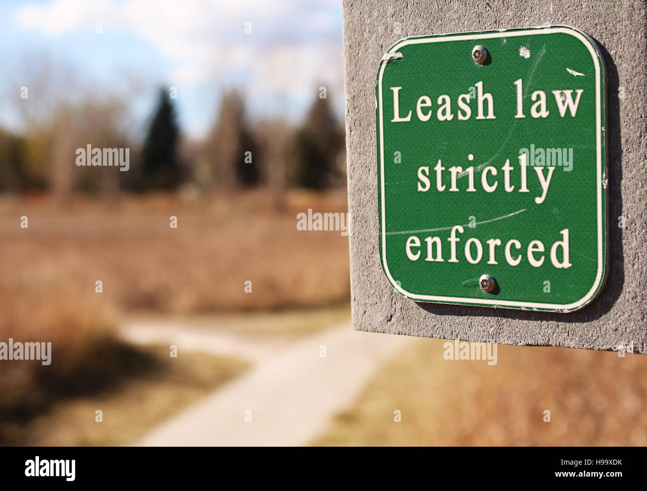 Sign along walking path warning that dog leash laws are strictly enforced. Stock Photo