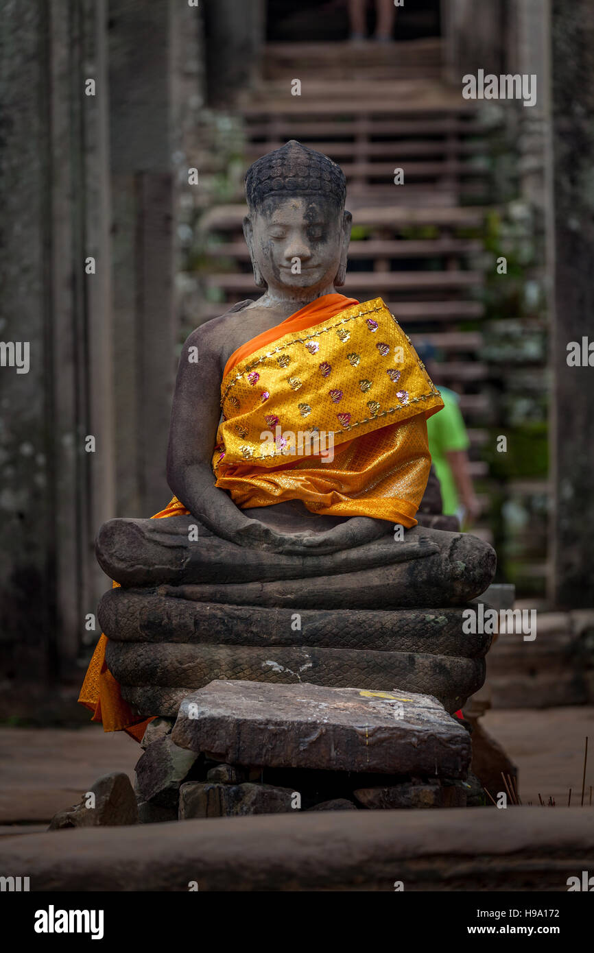Stone statue of Buddha wrapped with saffron and gold silk at Ta Prohm, Siem Reap, Cambodia. Stock Photo