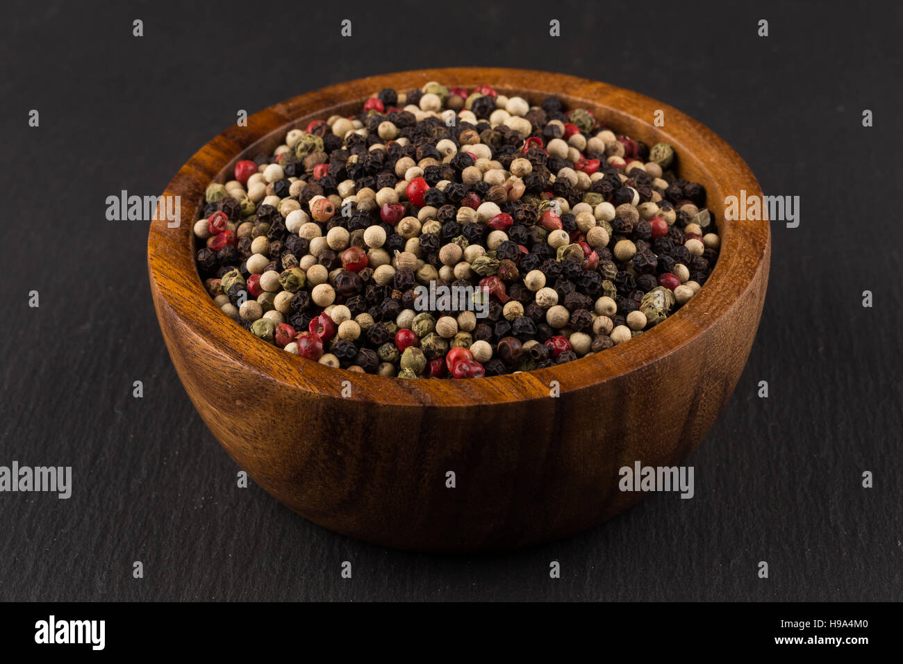 bowl of various pepper peppercorns seeds mix on black stone Stock Photo