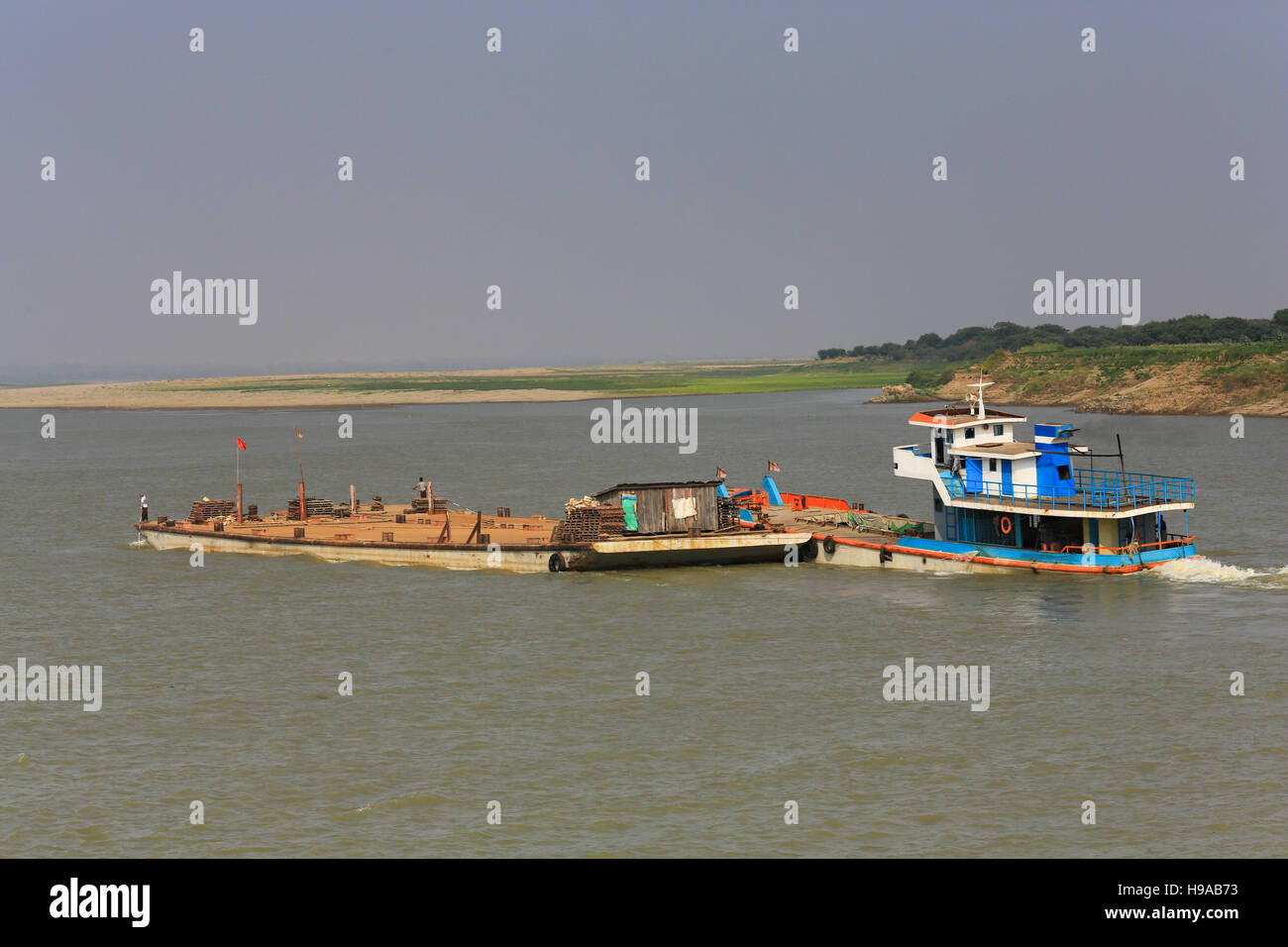 A river cargo boat heads upstream while pushing a barge on the