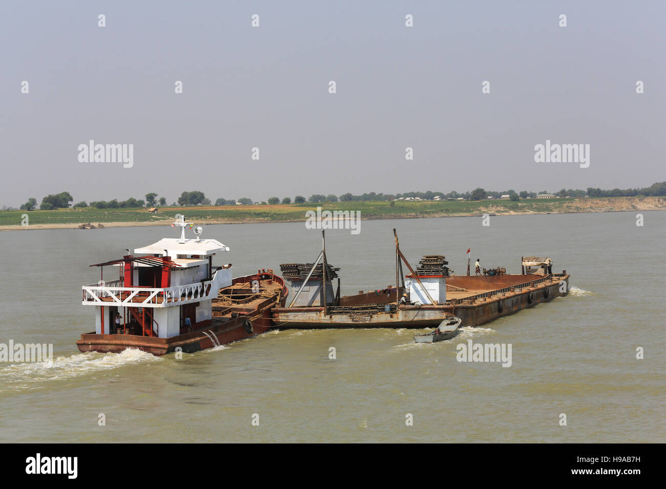 A river cargo boat heads upstream while pushing a barge on the