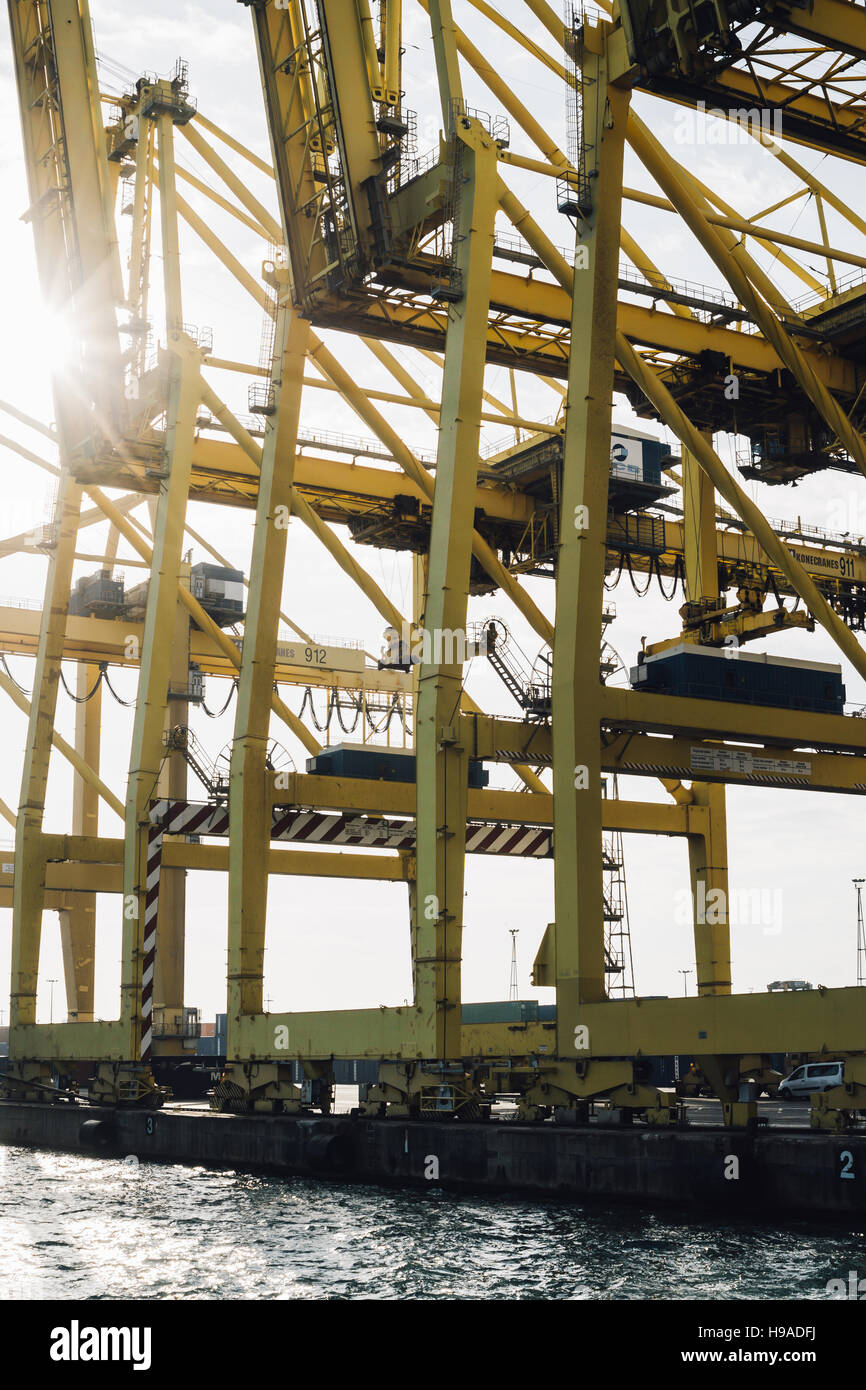 Yellow cranes at a port or harbour by the water, with a sun flare shining. Stock Photo