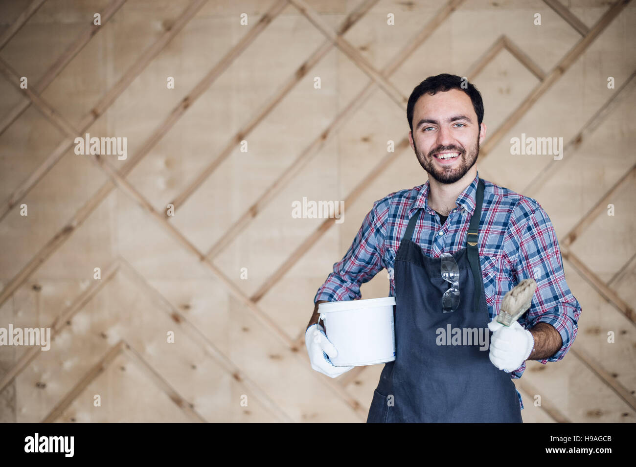 Young male carpenter wearing gloves and glasses with hands on hips Stock Photo