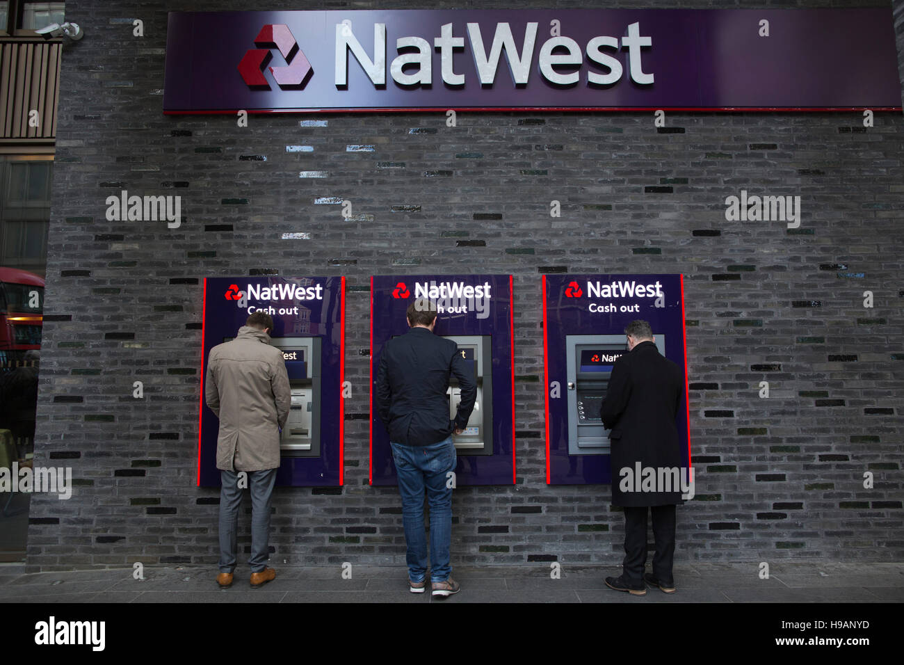 Three men making a cash withdrawal at NatWest banking cash dispensing machines, Victoria Street, Central London, England, UK Stock Photo