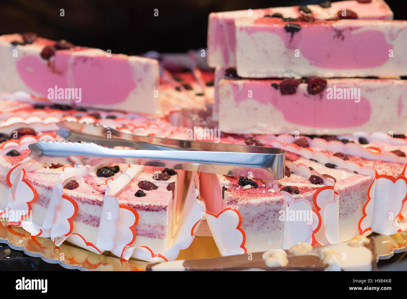 Close up artisan farmers market display of pink cherry berry cream cheese cake piled high with tongs Stock Photo
