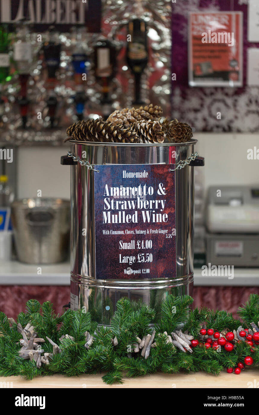 Vat of amaretto and strawberry mulled wine with green spruce, red holly berry decoration at christmas market stall Stock Photo