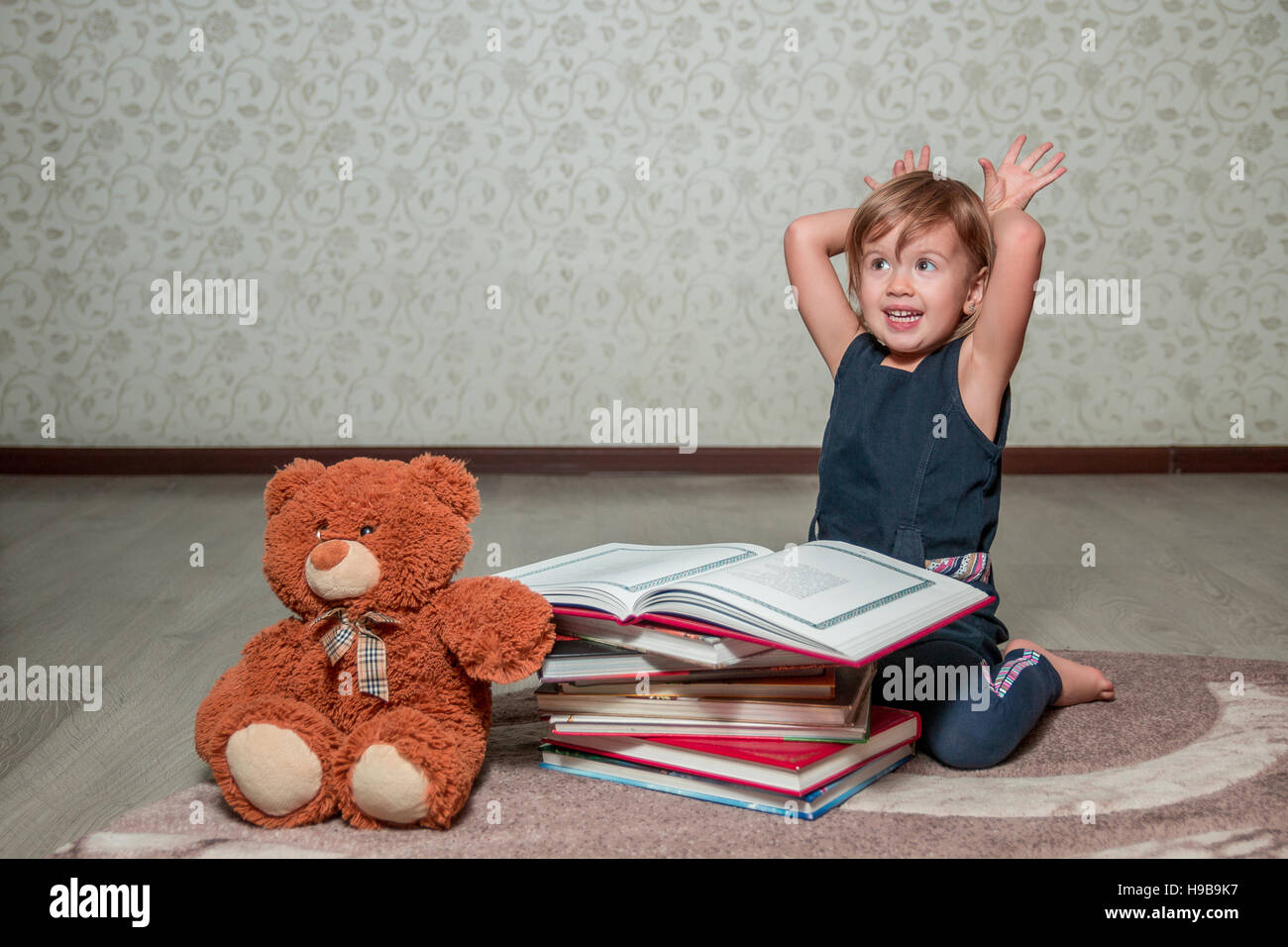 A little girl in a dark blue dress reading a book sitting on the floor ...