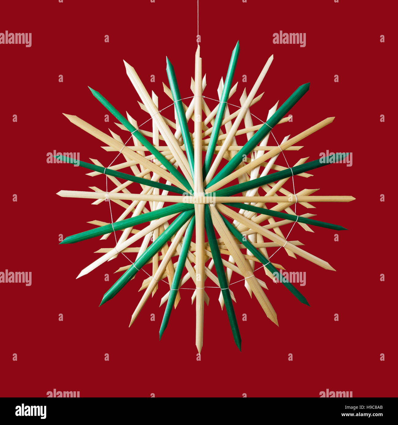 Straw star Christmas decoration on red background. Handmade colorful decor for windows, as gifts or to hang on the xmas tree. Stock Photo