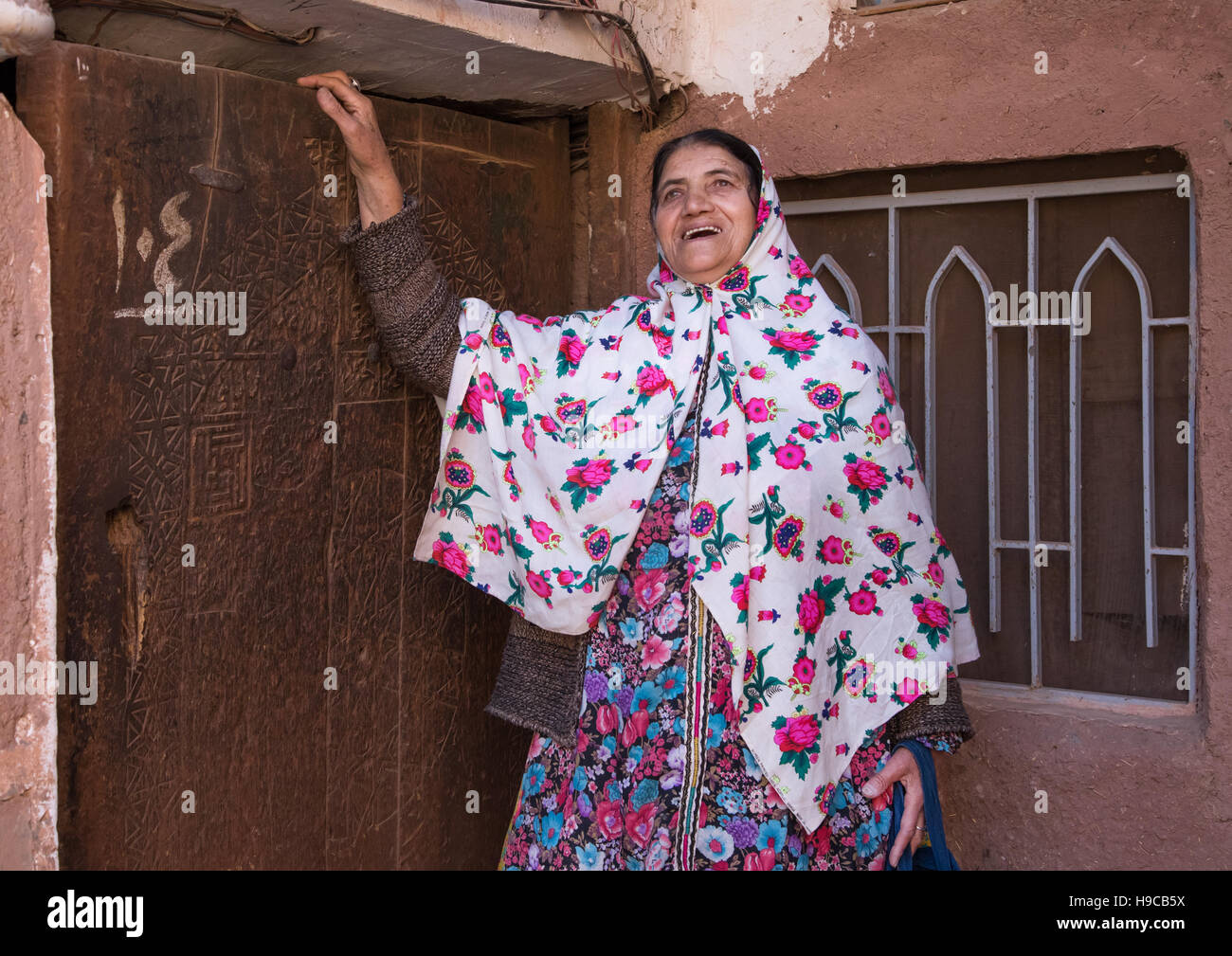 Portrait of an iranian woman wearing traditional floreal chador in front of an old wooden door, Natanz county, Abyaneh, Iran Stock Photo