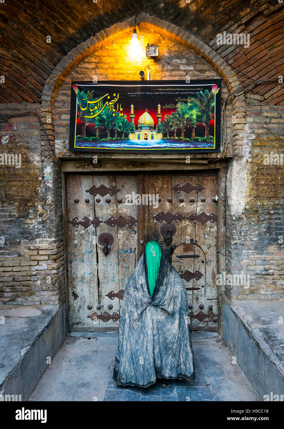 Iranian shiite muslim woman standing in front of an old wooden door after rubbing mud on her chador during the kharrah mali ritual to mark the ashura  Stock Photo