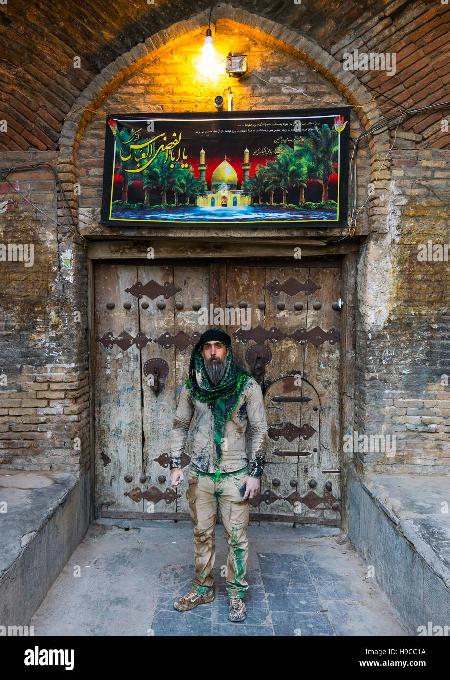 Iranian shiite muslim man standing in front of an old wooden door after rubbing mud on his clothes during the kharrah mali ritual to mark the ashura c Stock Photo