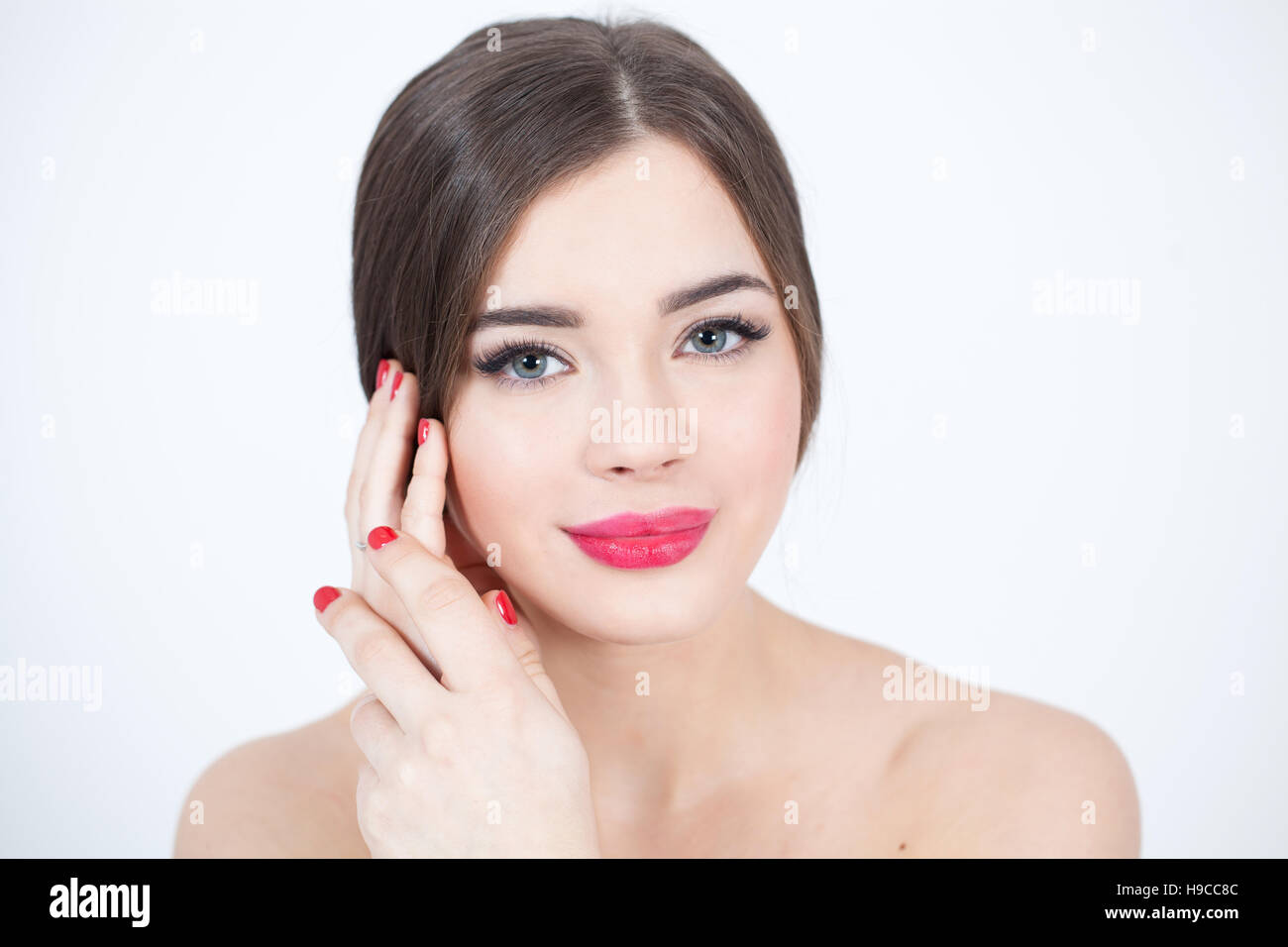 Beautiful Young Woman with Fresh Clean Skin touch own face. Red lips, red lipstick. Cosmetology, beauty and spa. Stock Photo