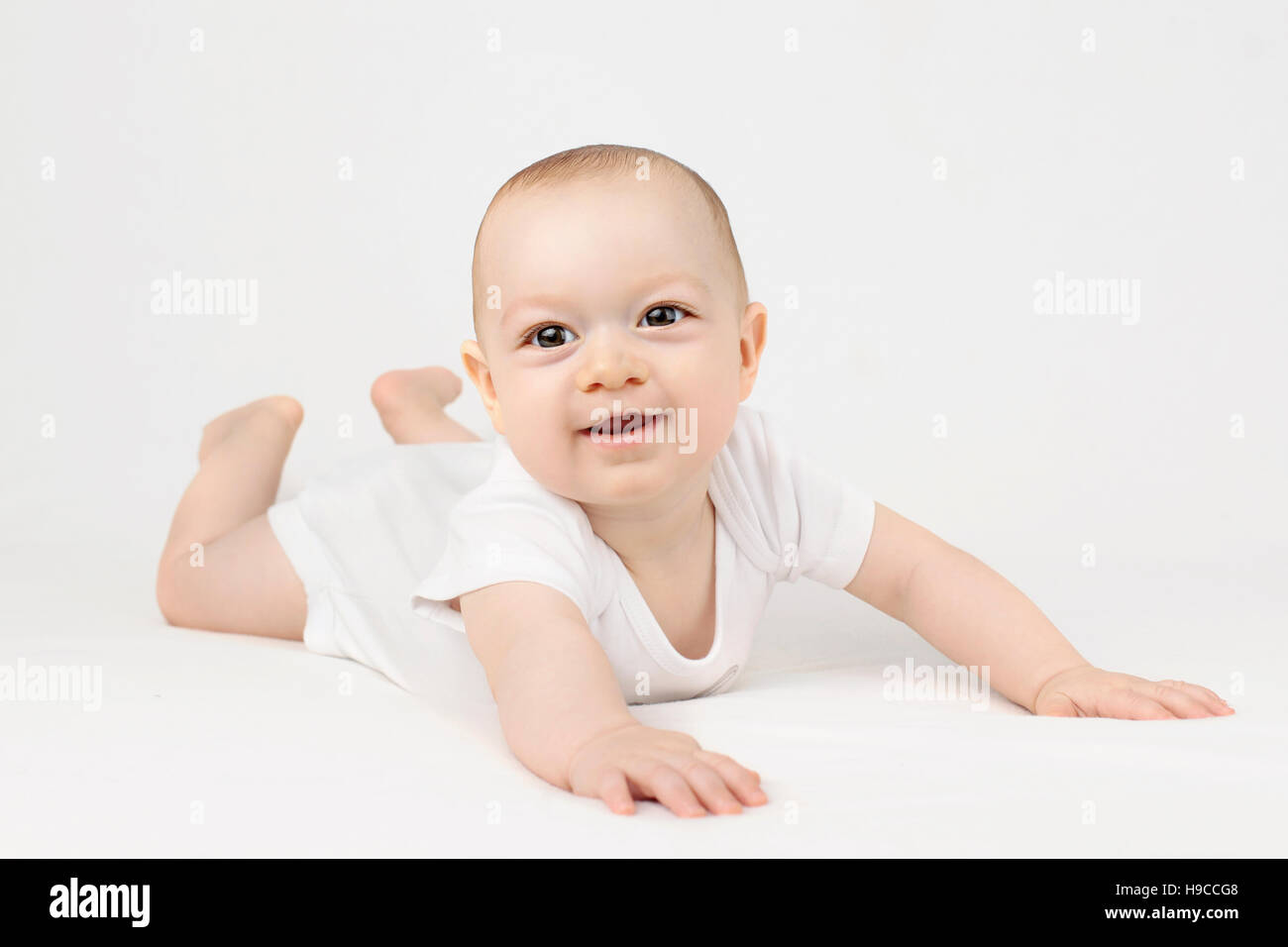 Baby boy lying down on his belly, smiling on the white background Stock Photo