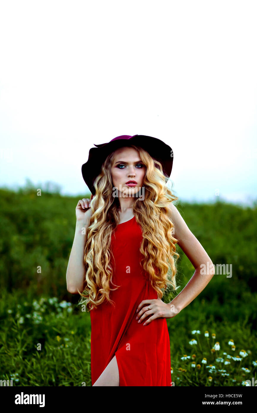 young beautiful girl in a red hat and red dress standing in the field ...