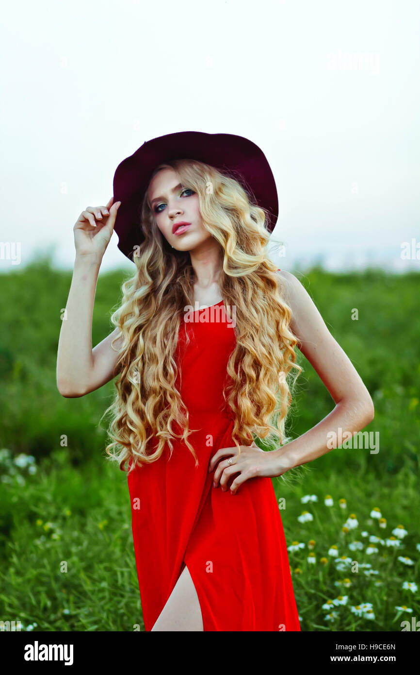 young beautiful girl in a red hat and red dress standing in the field ...