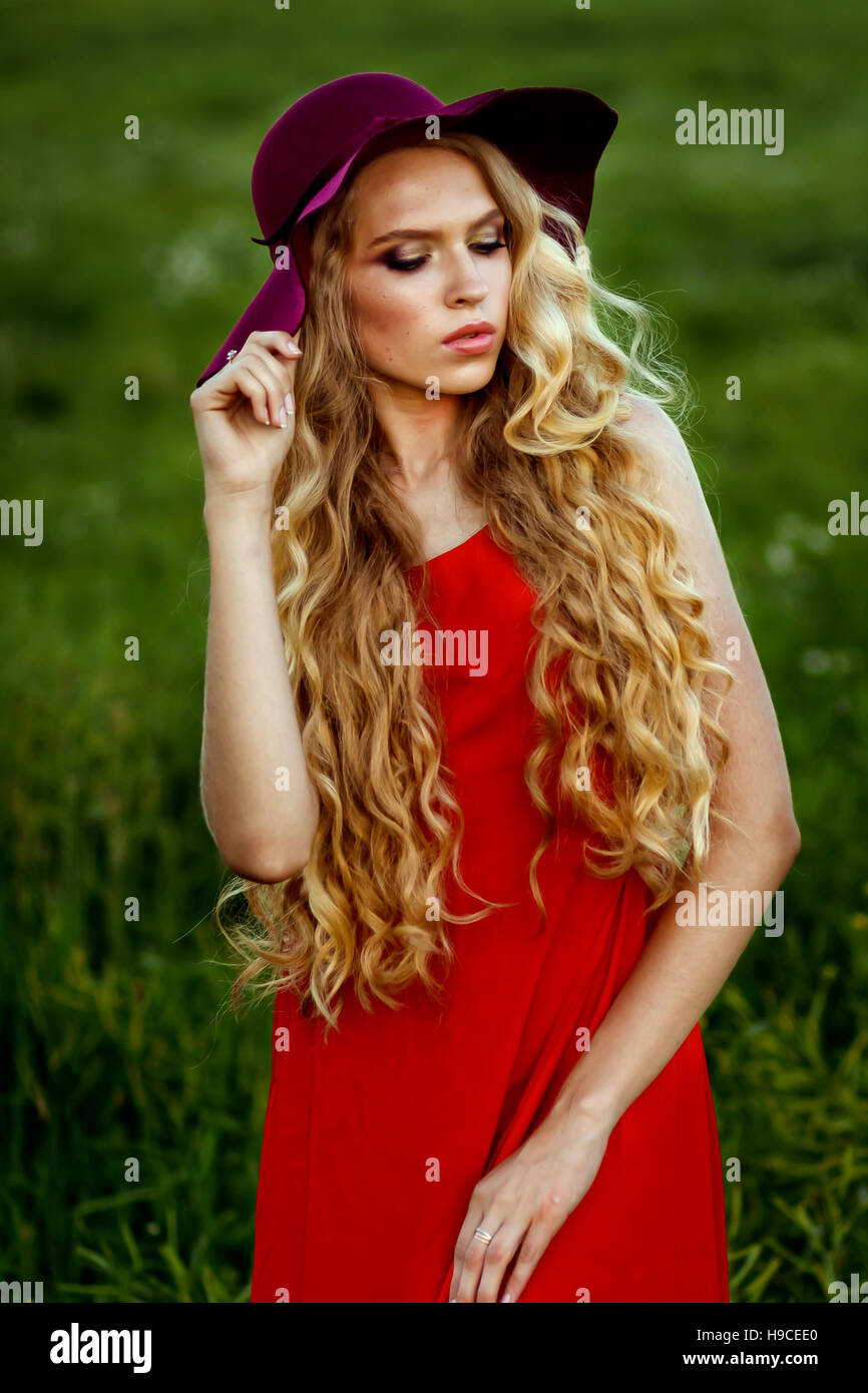 young beautiful girl in a red hat and red dress standing in the field ...