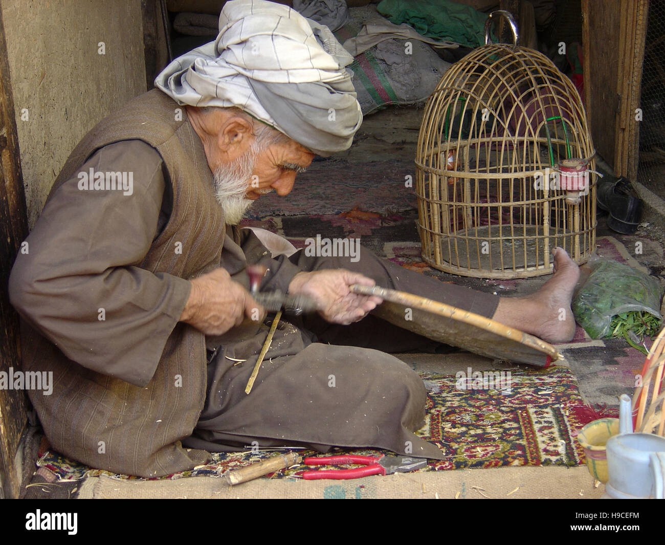 28th May 2004 An old man wearing a lungee (turban) makes wicker bird-cages inside the Ka Farushi bazaar in Kabul, Afghanistan. Stock Photo