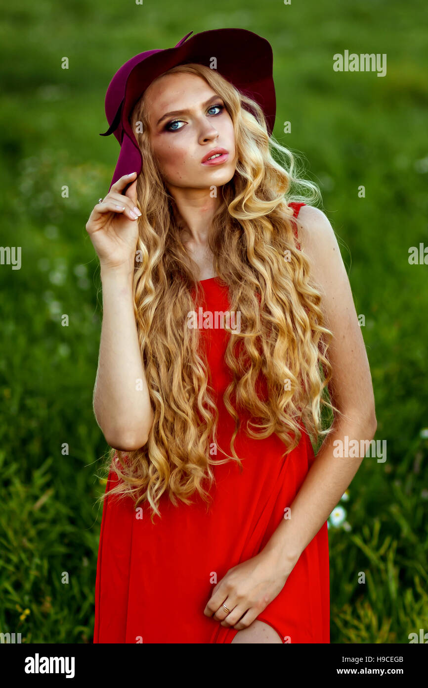 young beautiful girl in a red hat and red dress standing in the field ...