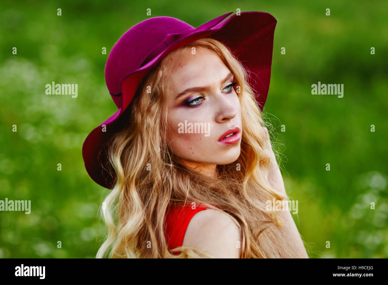 young beautiful girl in a red hat and red dress standing in the field ...