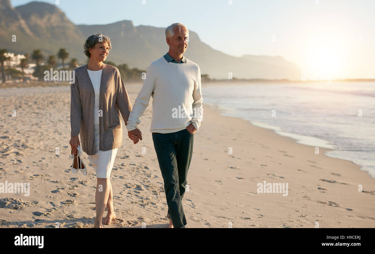 Shot of senior couple walking along beach together holding hands. Stock Photo
