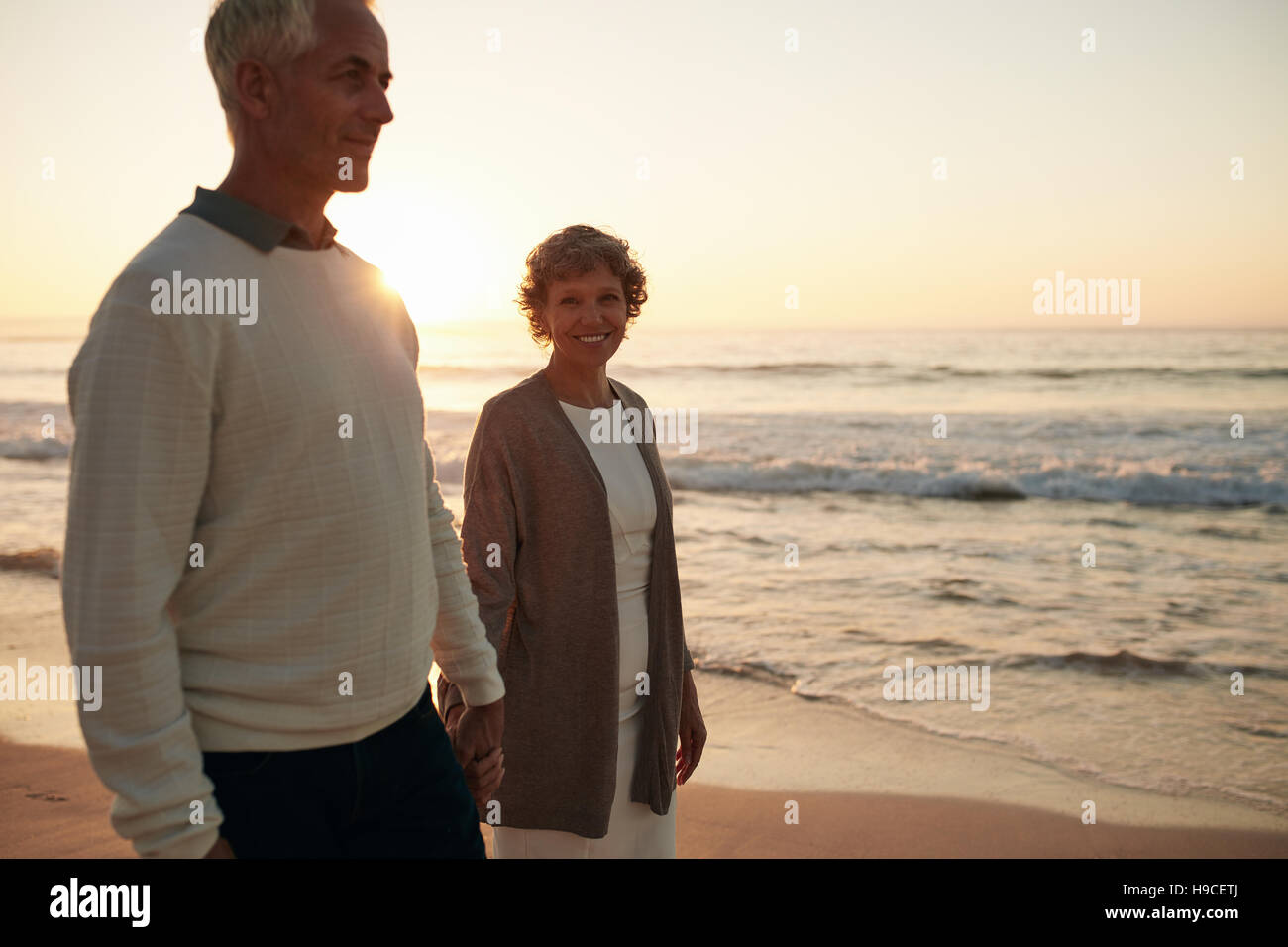 Senior woman with her husband strolling on the beach. Mature couple walking together by the sea. Stock Photo