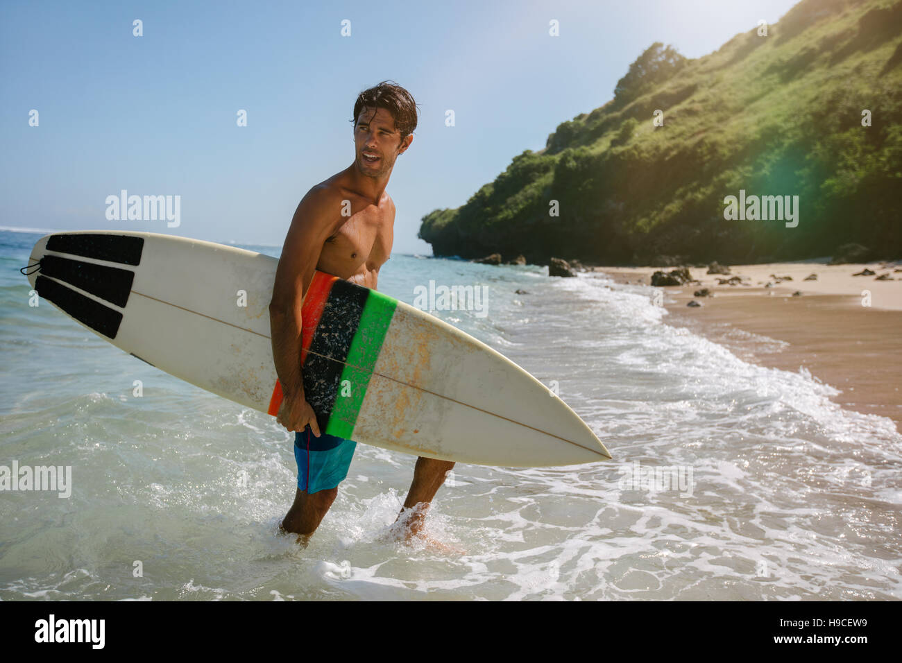Shot of handsome young man with surfboard on the beach. Male coming out of the sea after water surfing. Stock Photo