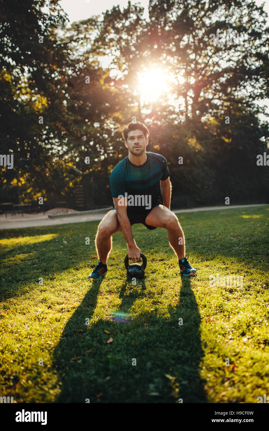 Vertical shot of strong young man exercising with kettle bell weights in the park.  Fit and muscular man training at park in morning. Stock Photo