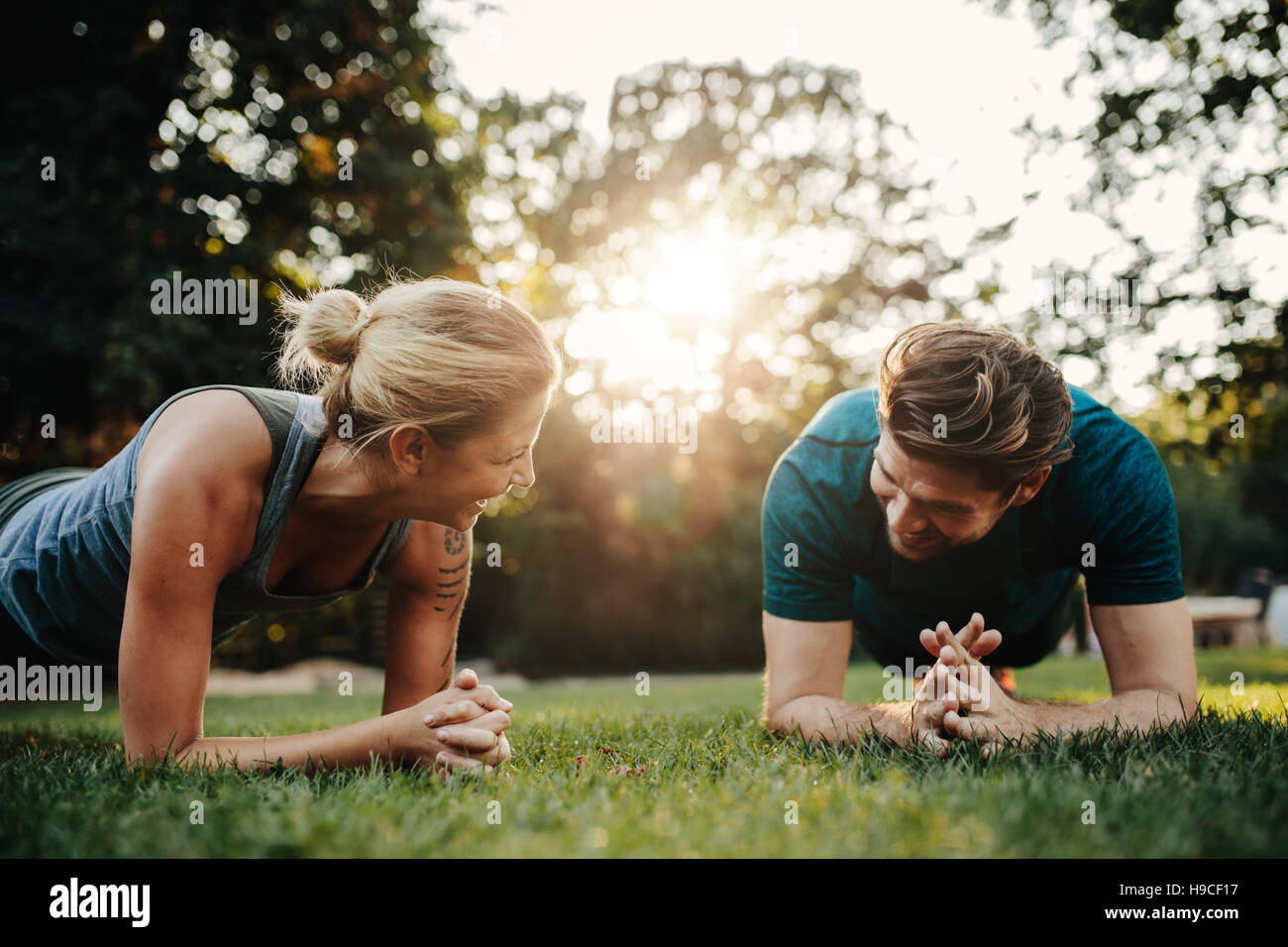 Caucasian couple doing core workout together in park. Fit young man and woman exercising. Stock Photo