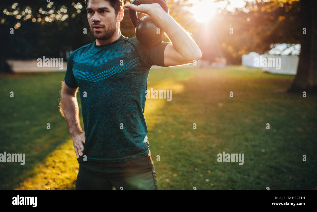 Shot of healthy young man working out with kettlebell. fitness male model training at park in morning. Stock Photo