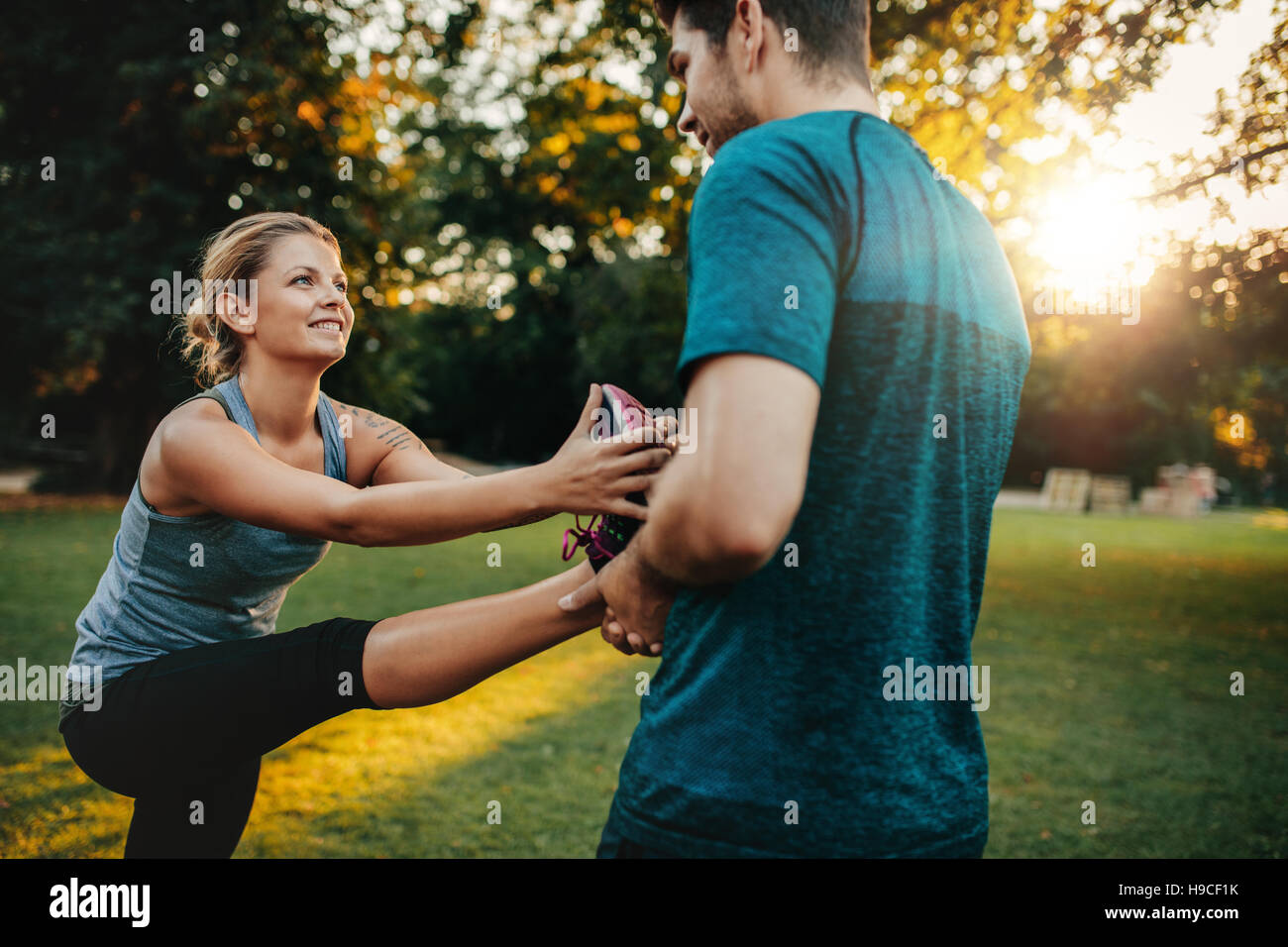 Male physical trainer assisting woman with leg exercise. Young woman being assisted by personal trainer in stretching exercises at park. Stock Photo