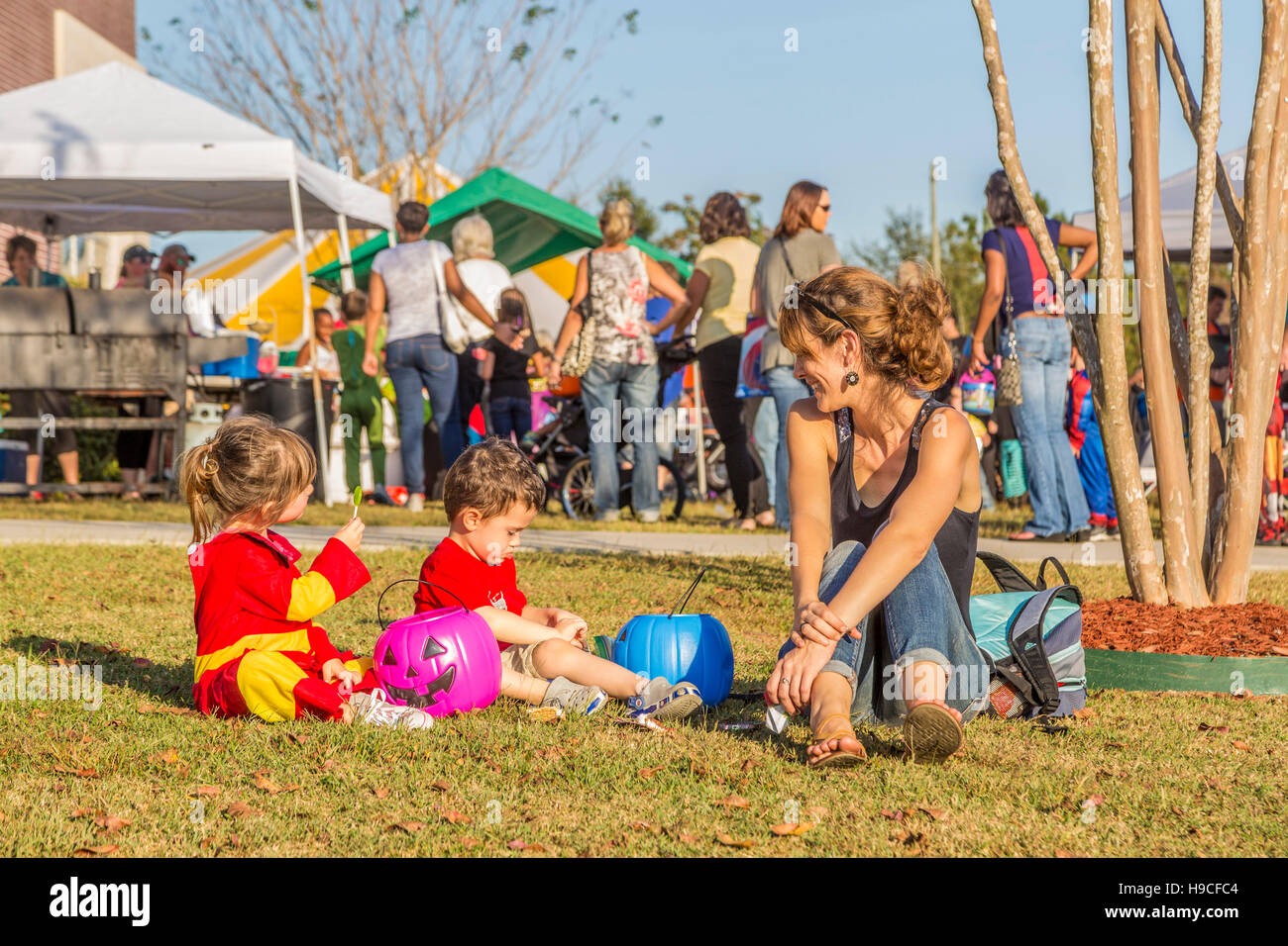 Young woman watches her children looking through their plastic pumpkins filled with candy at a Trunk or Treat fall festival at a Baptist church in MS Stock Photo