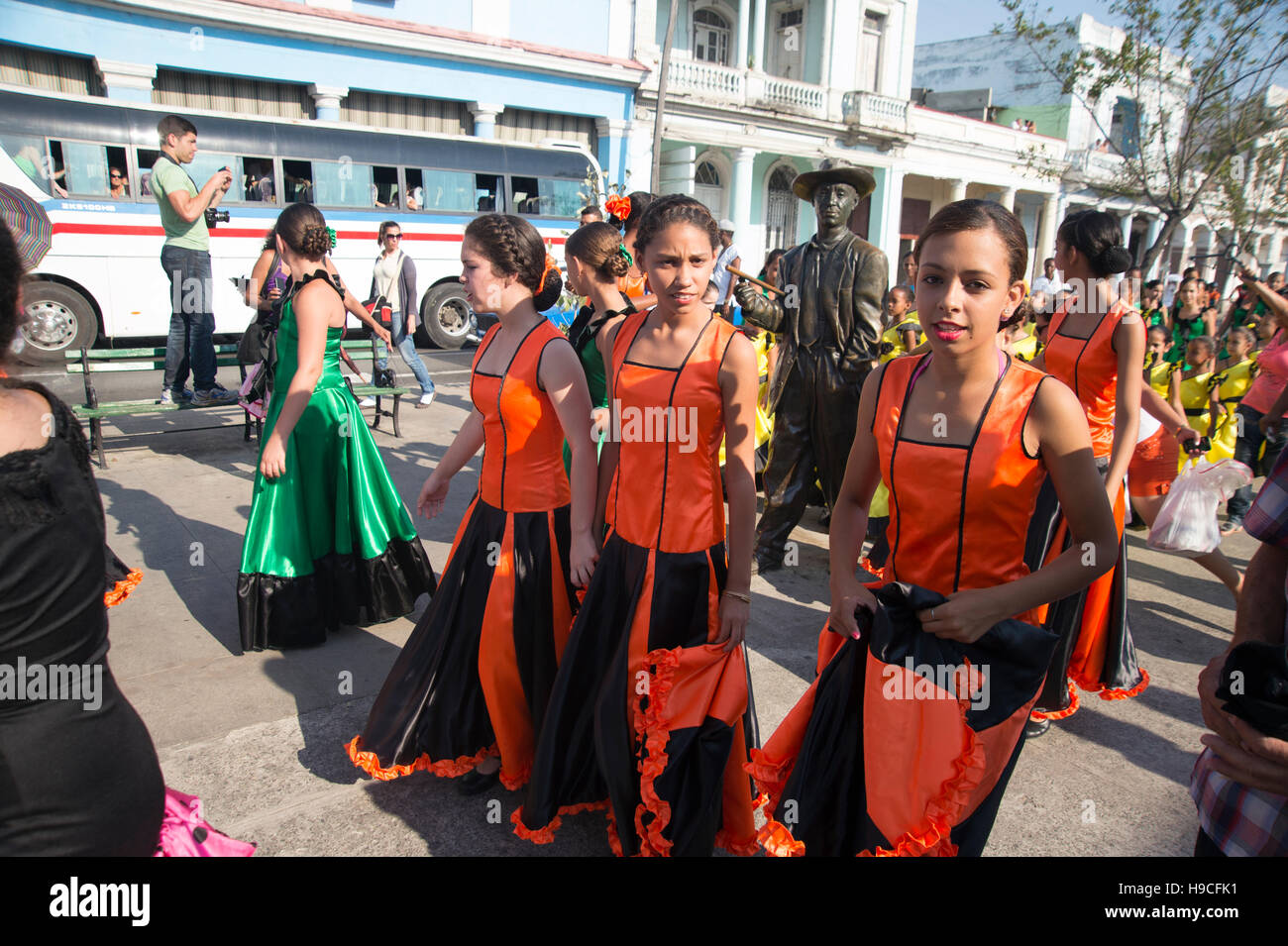 Young Cuban schoolgirls dressed in festival costume walk past the statue of Benny More in central Cienfuegos Cuba Stock Photo