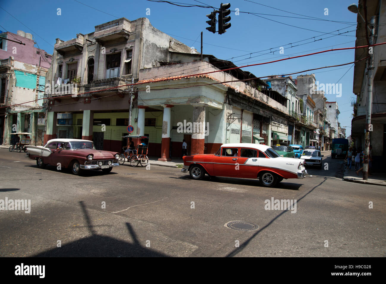 A busy intersection in Centro Havana with many old vintage US classic cars driving past crumbling architecture Cuba Stock Photo