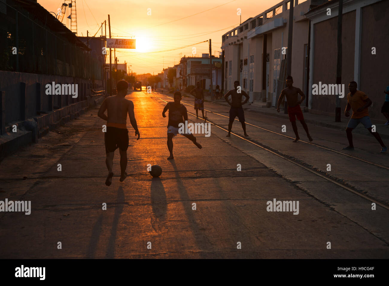 Silhouettes of Cuban teenagers playing football in the street as the sun sets behind them in Cienfuegos Cuba Stock Photo