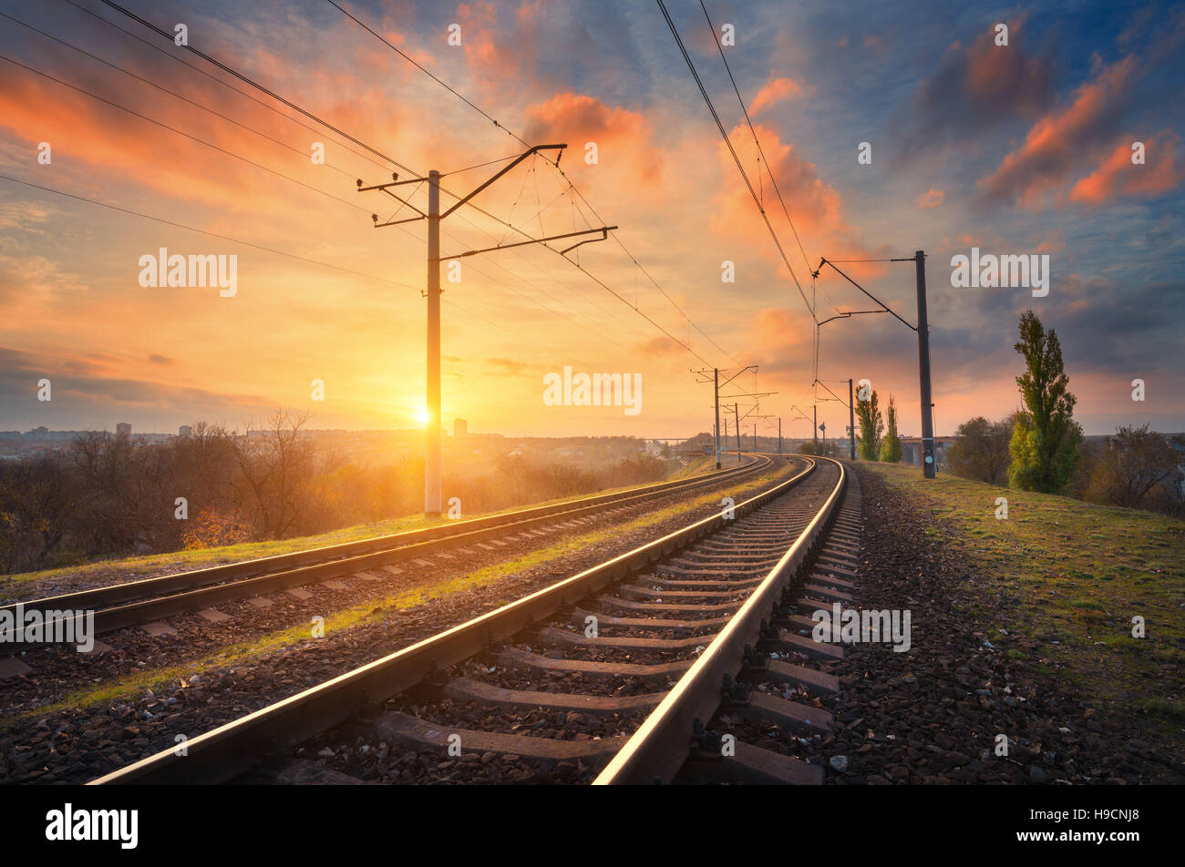 Railway station against beautiful sky at sunset. Industrial landscape with railroad, colorful blue sky with red clouds, trees Stock Photo