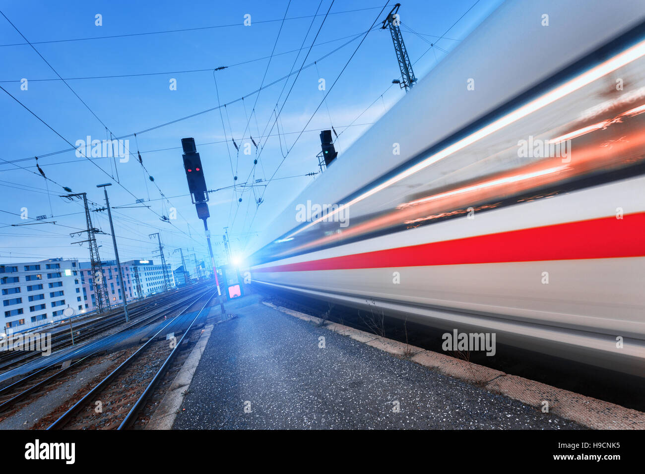 Modern high speed passenger train on railroad in motion at sunset. Blurred commuter train. Railway station at dusk. vintage Stock Photo
