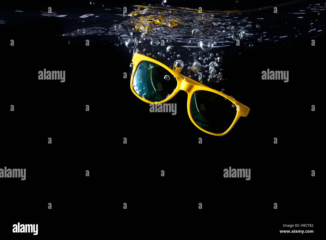 Yellow sunglasses splashing into water on black background. eyewear