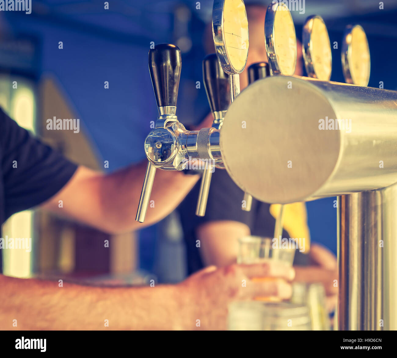 Barman hand at beer tap pouring a draught lager beer serving in a restaurant or pub.Vintage look Stock Photo