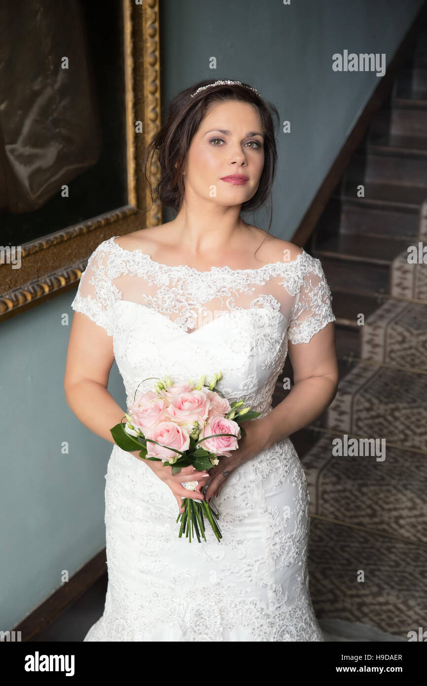 Bride in lace bridal gown holds pink bouquet, vertical format Stock Photo