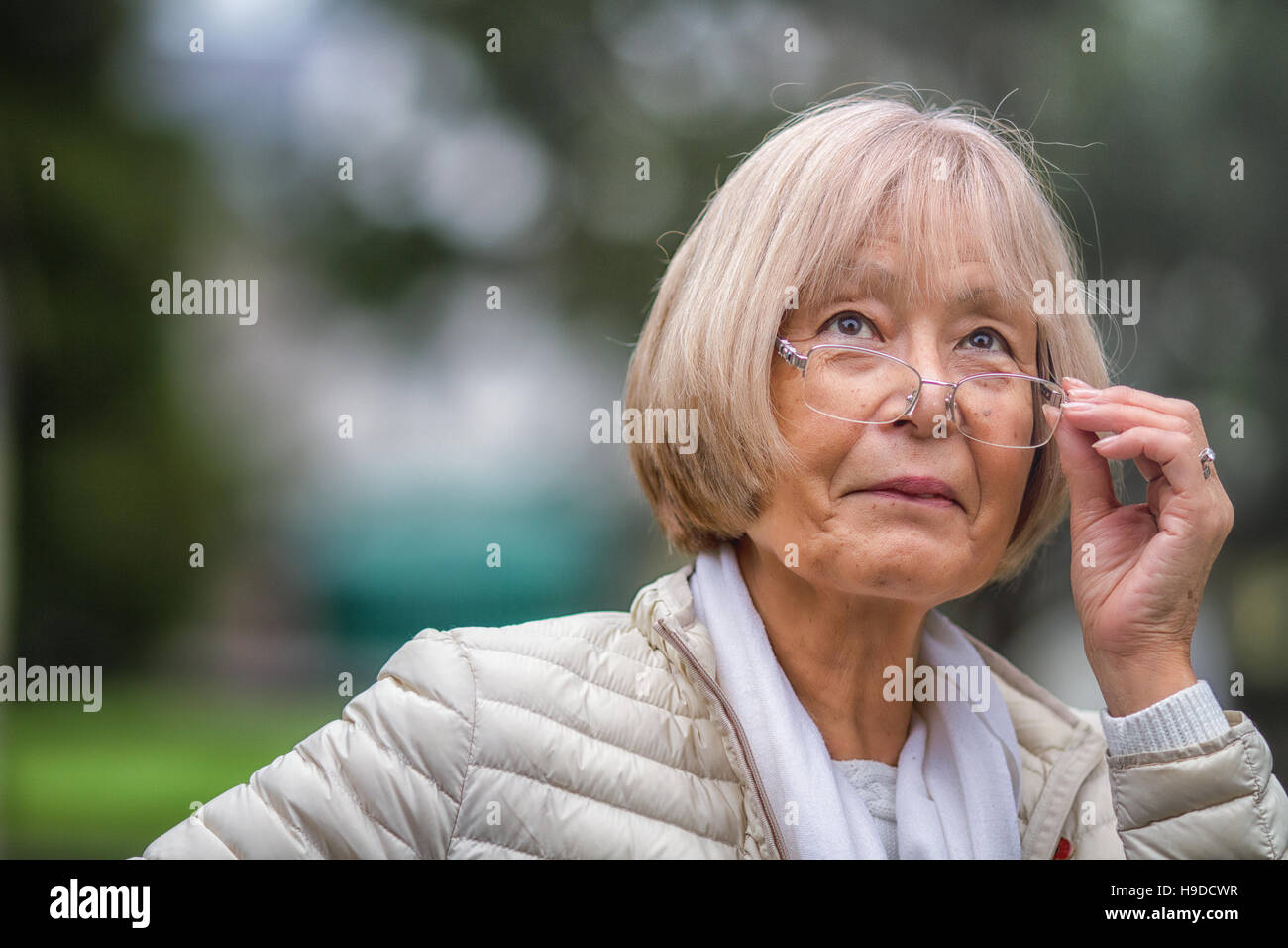 Elderly Japanese woman adjusts glasses whilst looking up Stock Photo