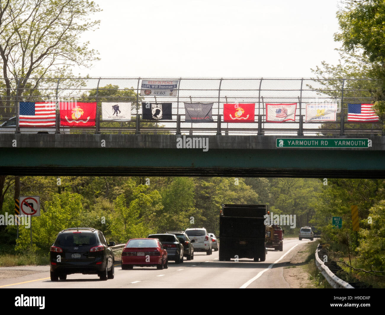 A US flag plus flags of US military services are displayed on a bridge over a Massachusetts highway in observance of Memorial Day. Note Prisoner of War (POW) flag in center. Stock Photo