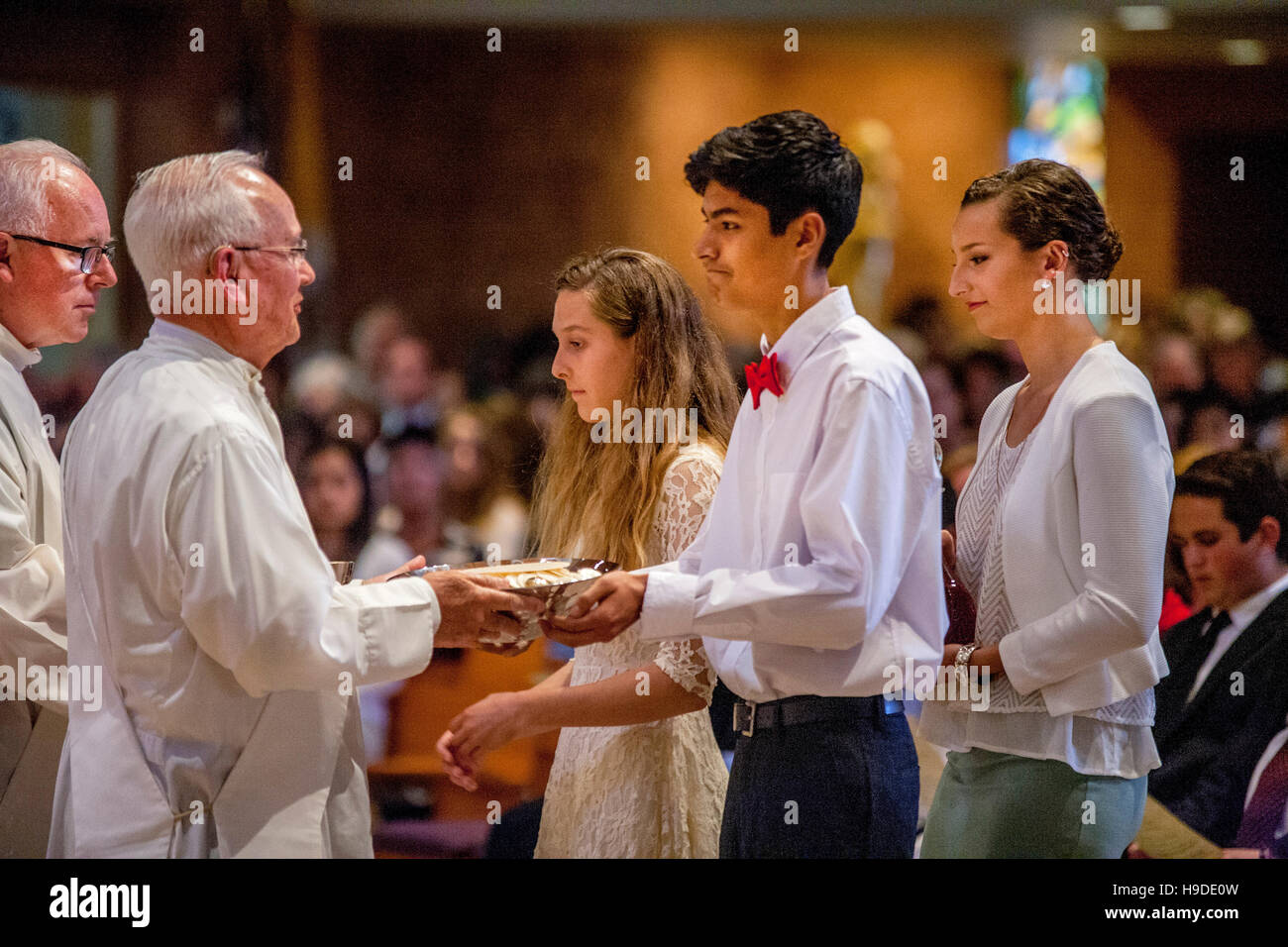 Teenage acolytes at a Catholic Church in Laguna Niguel, CA, bring filled collection baskets to a priest at the end of a mass. Note mother at right. Stock Photo